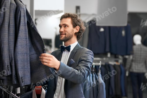 Preview: Young man choosing suits in boutique
