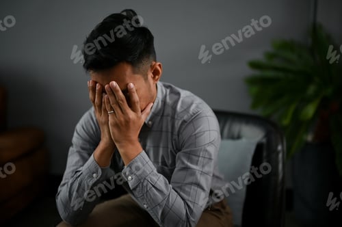 Preview: Stressed and depressed Asian man is covering his face, crying about his failures in life