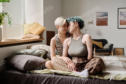 Preview: Lesbian couple sitting on bed in bedroom