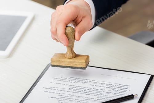 Preview: cropped view of realtor holding stamp near clipboard with document on table, leasing concept