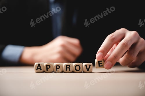 Preview: Closeup of wooden cubes with letters and word approve on table with unrecognized man