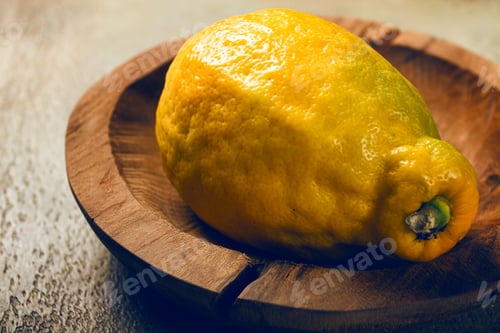 Preview: Bright yellow lemon resting on a wooden dish illuminated by soft light in a cozy kitchen setting