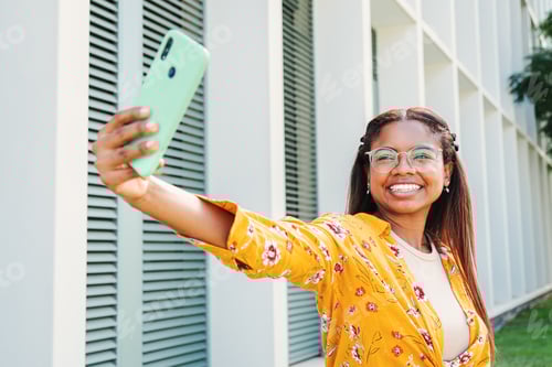 Preview: African american student woman smiling taking a selfie portrait with a cellphone, showing a toothy