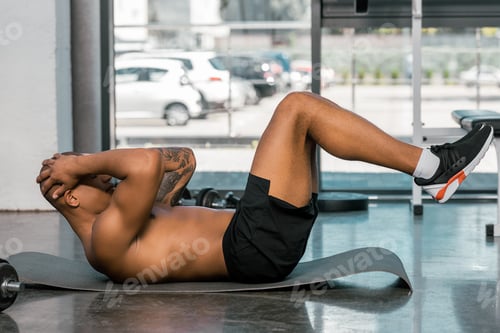 Preview: side view of african american sportsman doing abs on fitness mat at gym