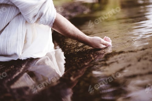Preview: Closeup shot of a person wearing a biblical robe while drinking water from the stream