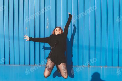 Preview: Woman in front of blue wall jumping in mid air