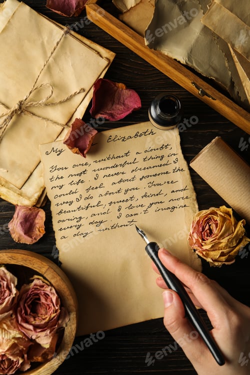 Preview: Letter with text, rose petals and ink pen in hand on wooden background, top view
