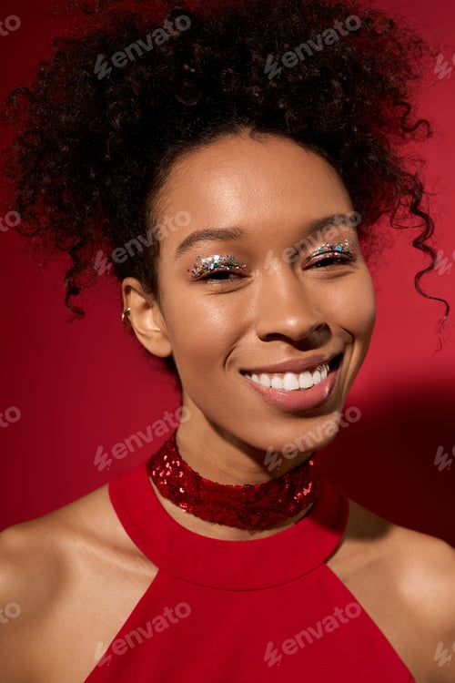 Preview: Young woman poses joyfully against a vibrant red backdrop with sparkling makeup