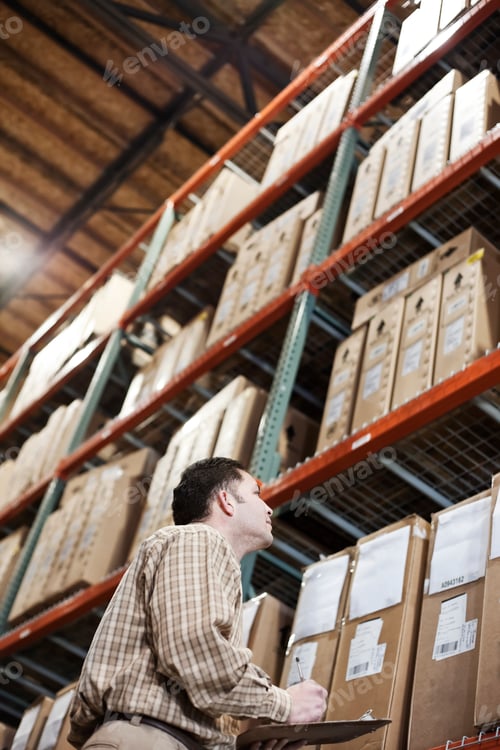 Preview: A storeroom manager looking at stock stacked high on shelves making notes with a clipboard and pen.
