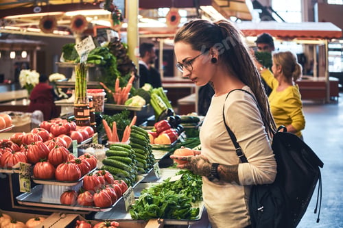 Preview: Tattooed young lady is choosing sesonal vegetables at market