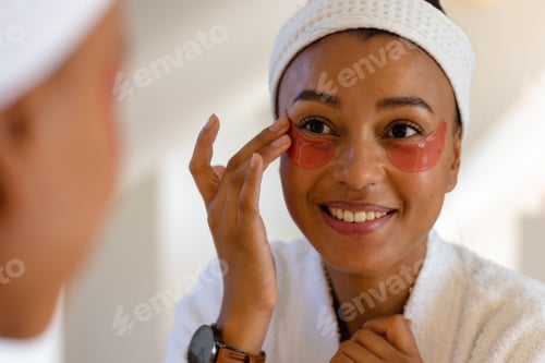 Preview: Happy biracial woman in bathrobe wearing eye mask in bathroom