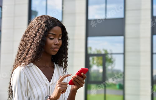 Preview: Young African woman model using mobile cell phone standing outdoors.