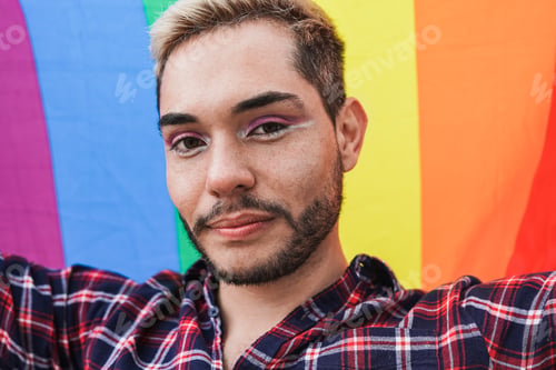Preview: Young gay man looking on camera while holding LGBT rainbwo flag