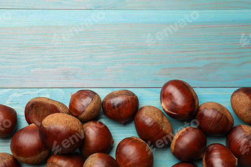 Preview: Roasted edible sweet chestnuts on light blue wooden table, flat lay. Space for text