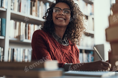 Preview: Positive Emotional Curly Student In Warm Sweater Holding A Pencil And Smiling While Sitting In The