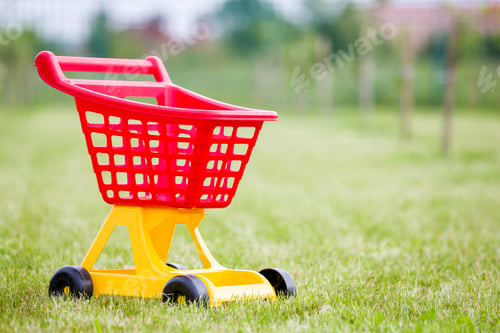 Preview: Bright plastic colorful shopping cart toy outdoors on sunny summer day.