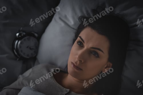 Preview: top view of awake woman with insomnia lying on bed near alarm clock