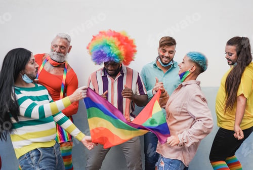 Preview: Multiracial people dancing at lgbt pride parade with rainbow flag while wearing safety mask
