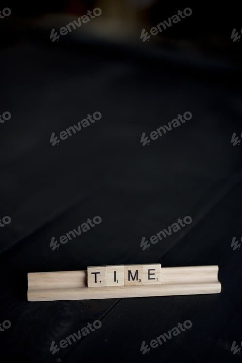 Preview: Vertical shot of wooden blocks spelling out time on a black wooden surface