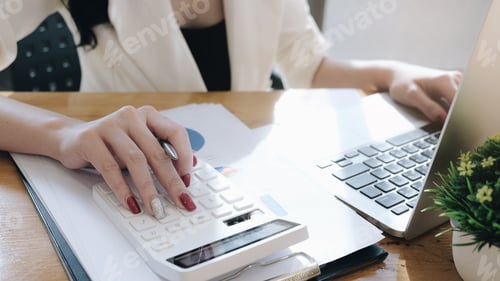 Preview: Close up Businesswoman using calculator and laptop for do math finance on wooden desk in office and