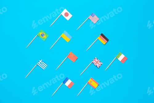 Preview: Many small paper flags of different countries on light blue background, flat lay