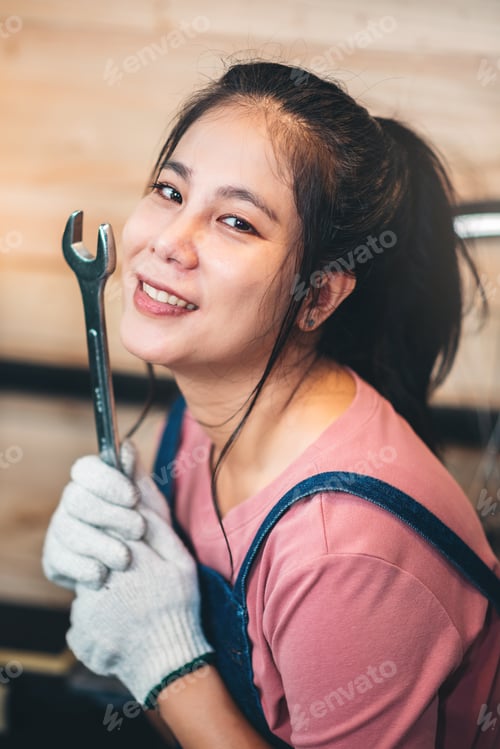 Preview: Smiling Asian woman conducting bike maintenance at home, focused on repairing the chain.