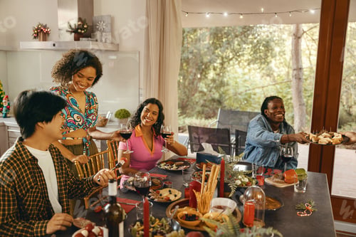 Preview: Group of smiling friends enjoying in conversation and drinking wine during Christmas party at home