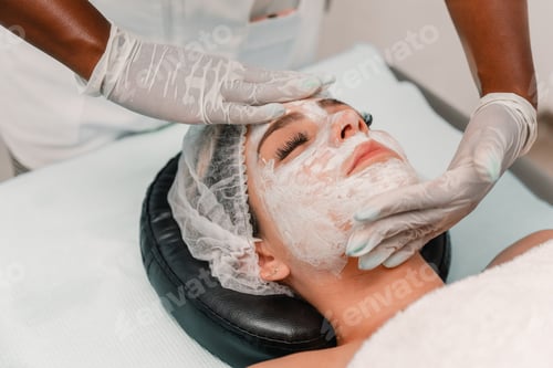 Preview: Close up of beautician applying moisturizing facial mask on woman’s face during beauty treatment