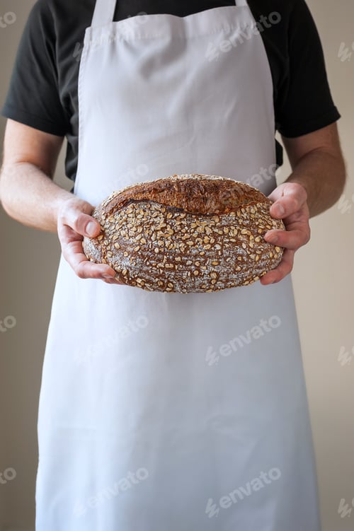 Preview: Close-up at bakers hands holding a loaf of bread in front of him.