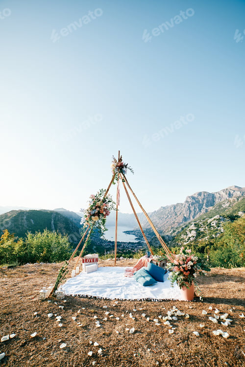 Preview: Wedding wigwam arch with a blanket and pillows stands in a clearing on a mountain above the Bay of