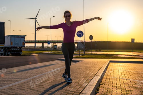 Preview: Dark silhouette of a young woman standing on empty parking lot at sunset
