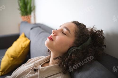 Preview: mixed race woman girl is sitting lying on couch at home with her eyes closed with headphones.