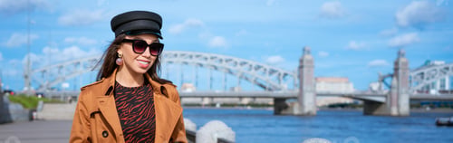 Preview: Happy young woman in light coat on the embankment posing