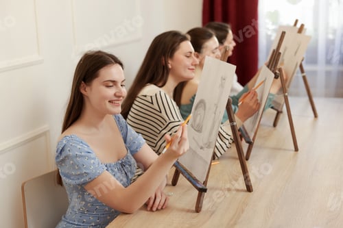 Preview: Group of women with easels learning to draw at wooden table in class