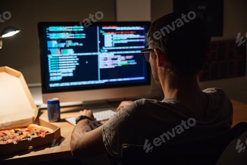 Preview: Back view of focused programmer writing code and eating pizza