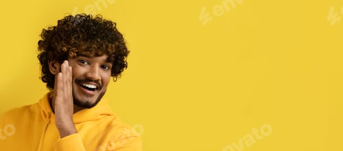 Preview: Cheerful hindu guy sharing secret, copy space on yellow