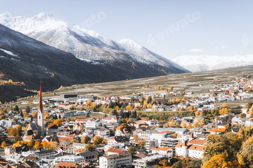 Preview: Aerial view of a small town in autumn foliage on the background of beautiful snowy mountains