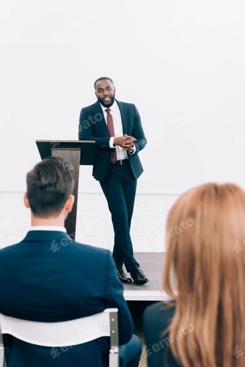 Preview: handsome african american speaker leaning on podium tribune during seminar in conference hall