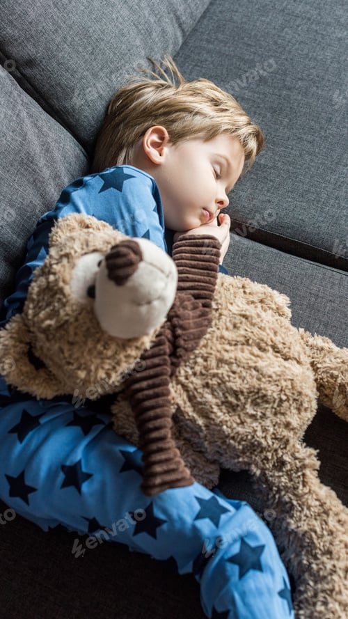 Preview: high angle view of adorable child sleeping on sofa with teddy bear