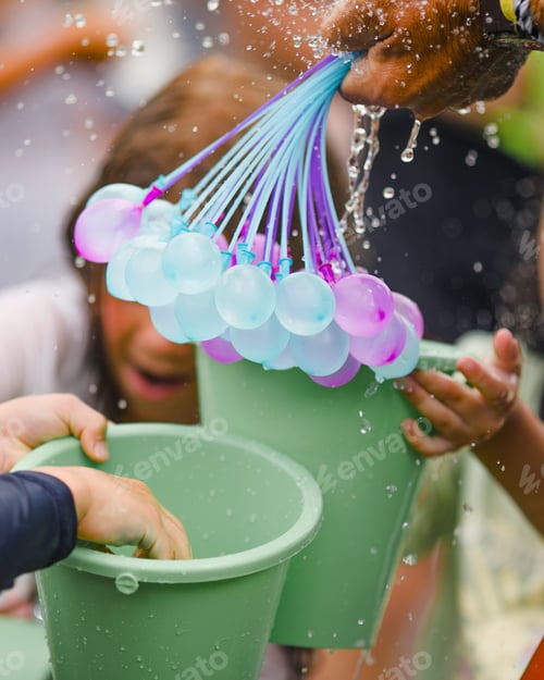Preview: colorful water bombs in summer ready to play. Holding balloons in hand.