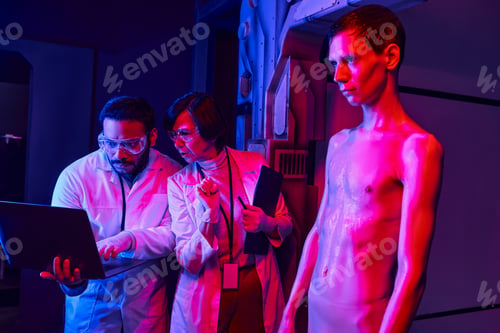 Preview: indian scientist pointing at laptop near colleague and extraterrestrial humanoid in science center