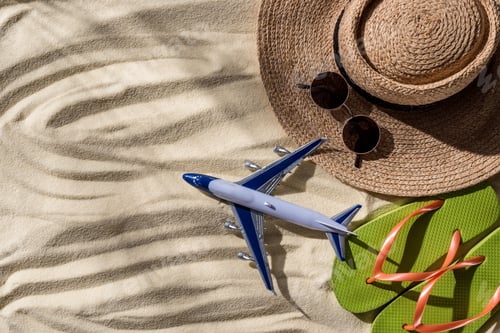 Preview: top view of toy plane, straw hat, flip flops and sunglasses on wavy sand with copy space