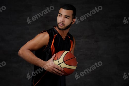 Preview: Young African-American basketball player in sportswear in a dark studio