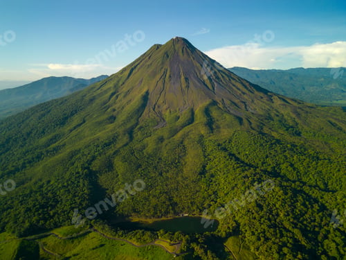 Preview: Aerial view of Arenal Volcano in Costa Rica surrounded by lush green forest under a clear blue sky