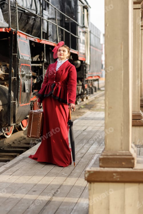 Preview: A girl in a burgundy suit and a hat with a veil stands with an umbrella near an old steam locomotive