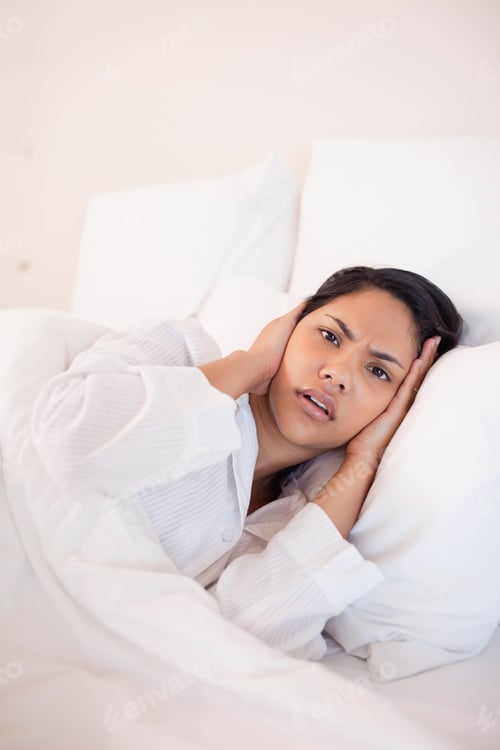 Preview: African American and Asian woman reclining on duvet in bedroom leaning on pillows pressing ears