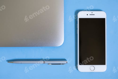 Preview: Flatlay view looking down at a silver computer laptop apple phone pen on a blank blue background bac