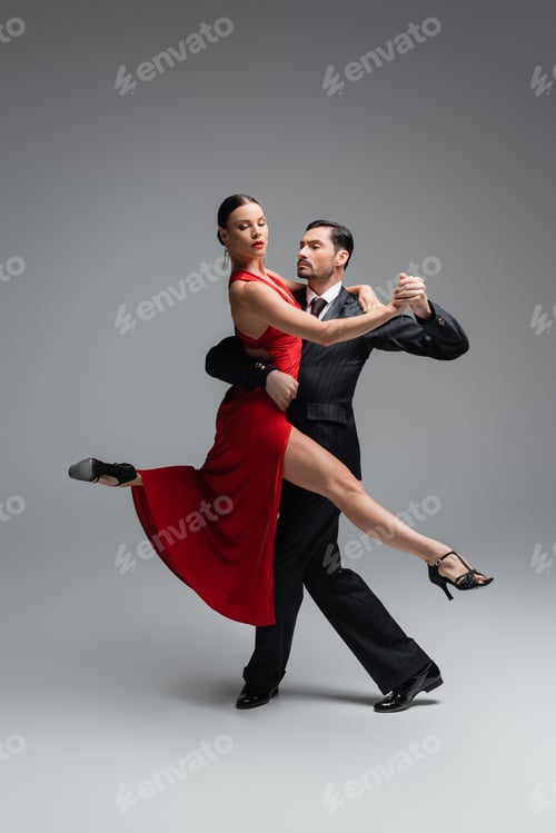 Preview: Stylish woman in red dress dancing tango with man on grey background