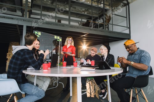 Preview: portrait of young business woman in red shirt at modern startup office interior, team in meeting