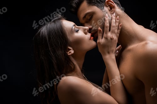 Preview: Side view of beautiful naked woman kissing shirtless man isolated on black